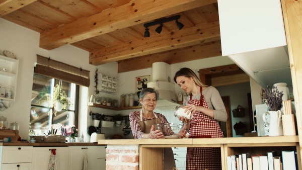 A happy elderly grandmother with an adult granddaughter putting flour in a bowl at home. Slow motion.