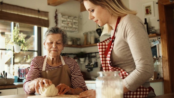 A happy elderly grandmother with an adult granddaughter at home, baking.