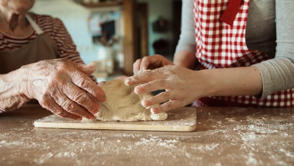 An unrecognizable elderly grandmother with an adult granddaughter at home, baking.