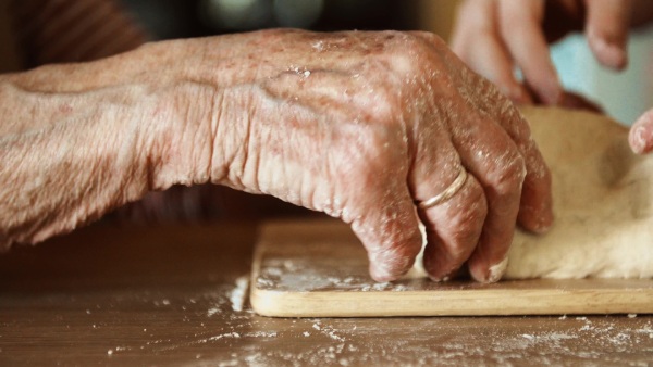 An unrecognizable elderly grandmother with an adult granddaughter at home, baking.