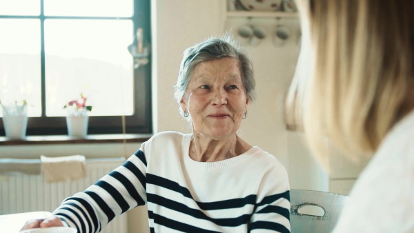 Portrait of an elderly grandmother with an unrecognizable adult granddaughter at home, talking. Slow motion.