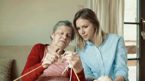 An elderly grandmother and adult granddaughter at home, knitting. Slow motion.