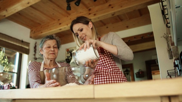 A happy elderly grandmother with an adult granddaughter at home, baking. Slow motion.