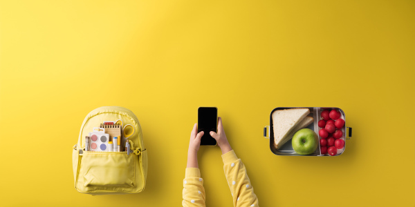 A flat lay top view of child hands with smartphone, healthy snack and back to school concept.