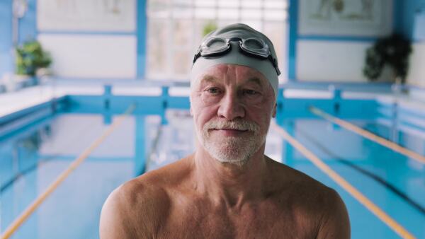 Senior man in an indoor swimming pool. Active pensioner enjoying sport.