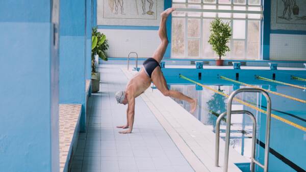 Senior man standing by the indoor swimming pool, stretching. Active pensioner enjoying sport.