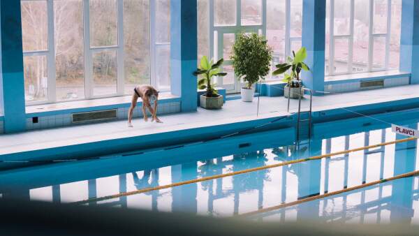 Senior man standing by the indoor swimming pool, stretching. Active pensioner enjoying sport.