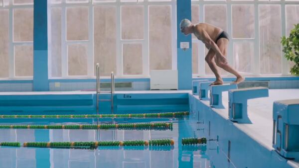 Senior man in an indoor swimming pool. Active pensioner enjoying sport. An old man jumping in the pool. Slow motion.