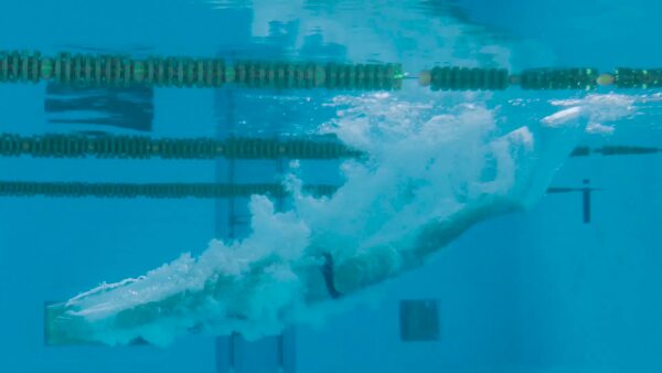 Senior man in an indoor swimming pool. Active pensioner enjoying sport. An old man jumping in the pool. Slow motion.