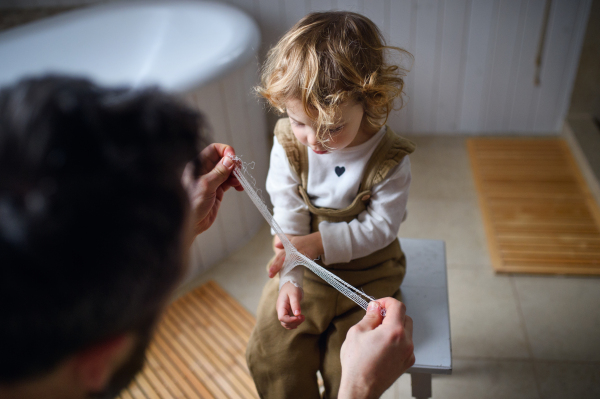 Unrecognizable father putting bandage on small hurt toddler child indoors at home.