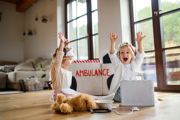 Two cheerful small children with doctor uniforms indoors at home, having fun when playing.