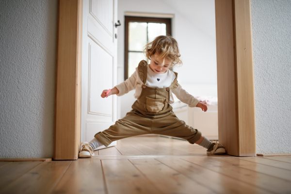 Front view of small toddler girl standing indoors at home, having fun.