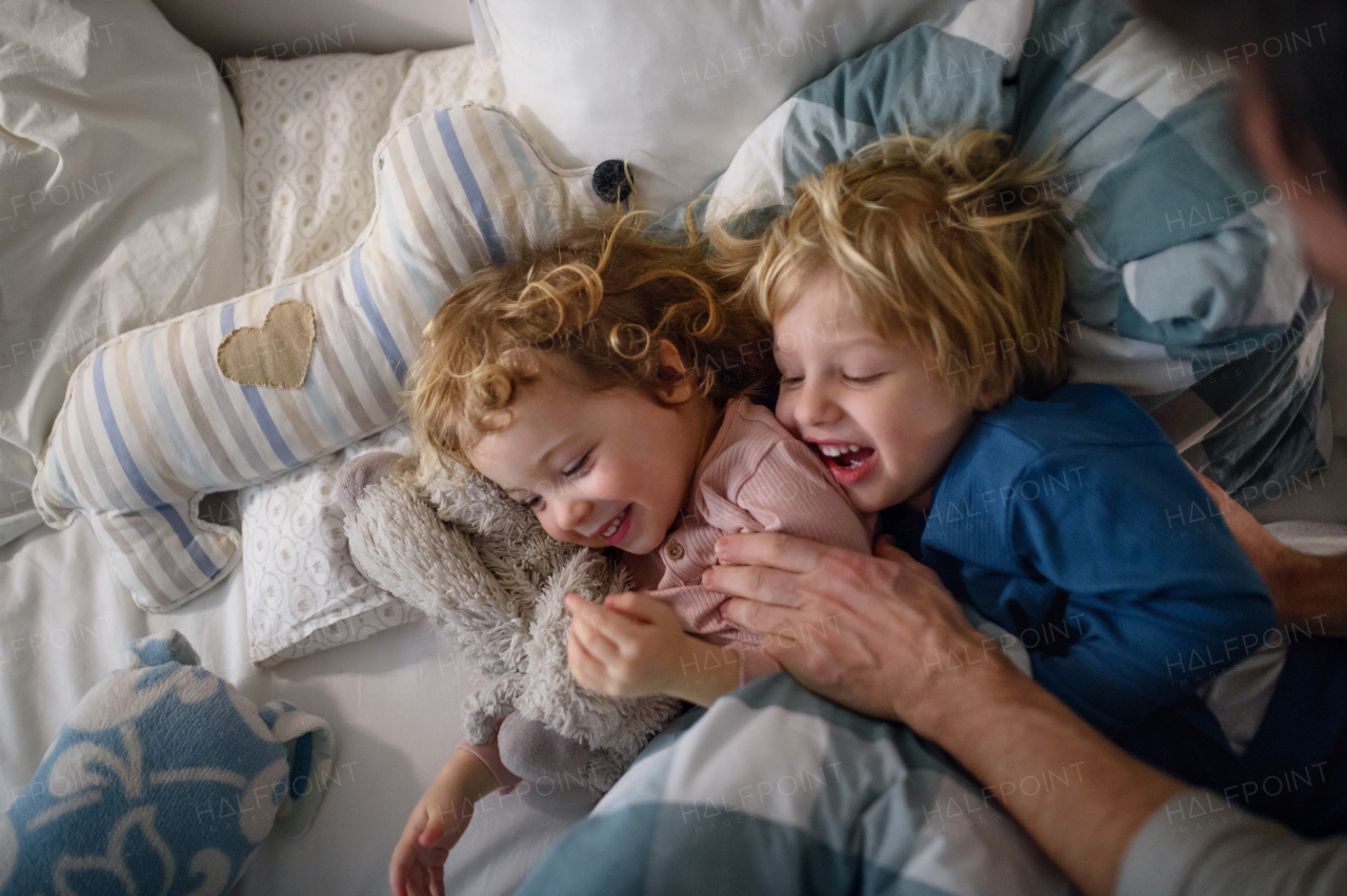 Two cheerful small laughing children with unrecognizable father at home, having fun.