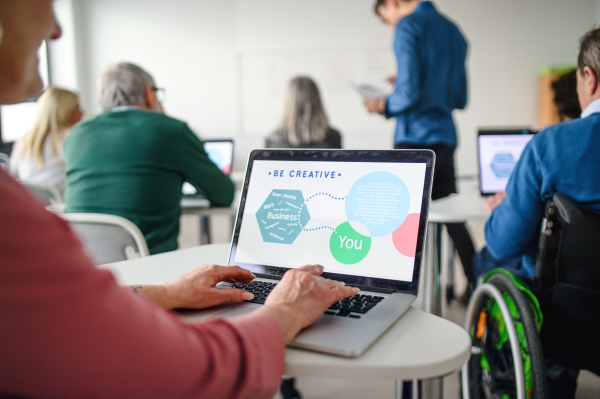 Rear view of group of senior people attending computer and technology education class.