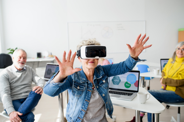 Group of cheerful seniors with VR goggles on computer and technology education class.