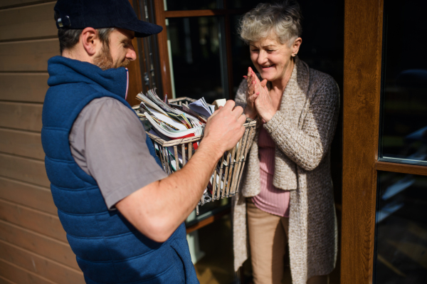 Man courier delivering books and magazines to senior woman, standing by doorstep.