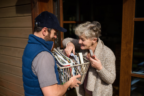 Man courier delivering books and magazines to senior woman, standing by doorstep.