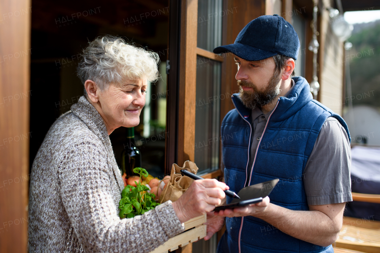 Man courier delivering shopping to senior woman, electronic signing.