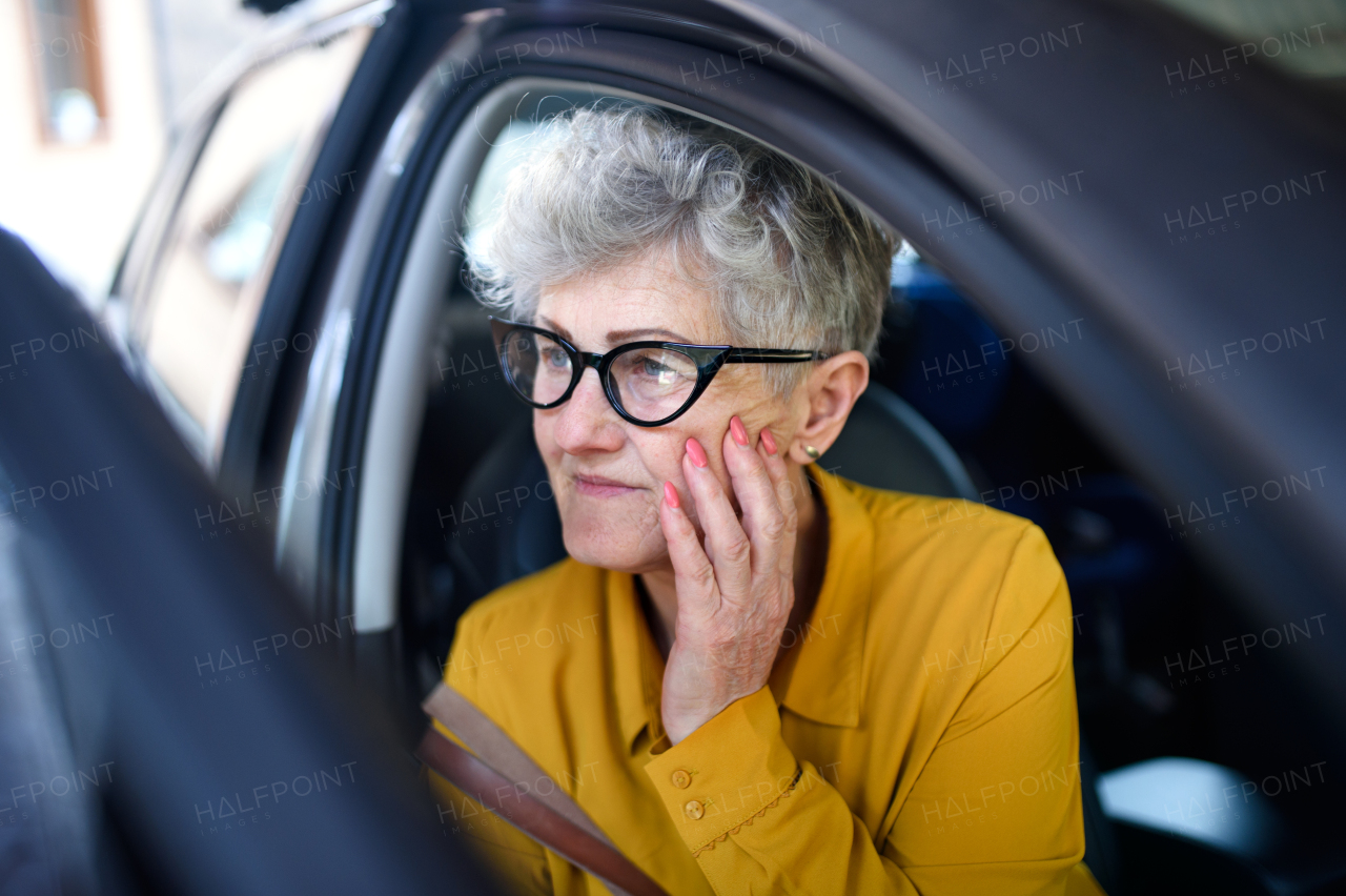 Sad senior woman with glasses getting out of a car.