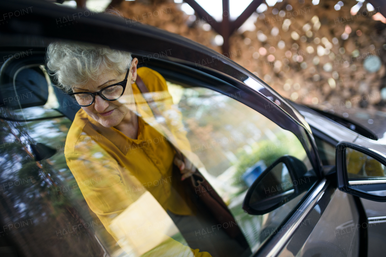 Sad senior woman with glasses getting out of a car. Shot through glass.