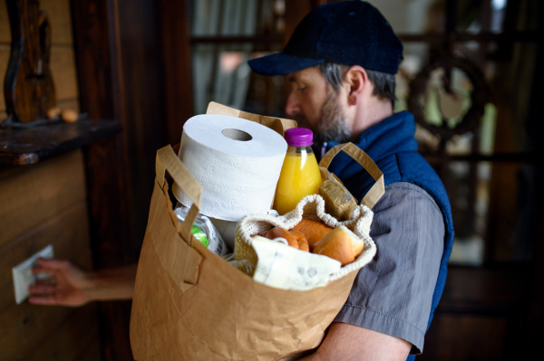 Man courier standing by front door and delivering shopping, knocking.