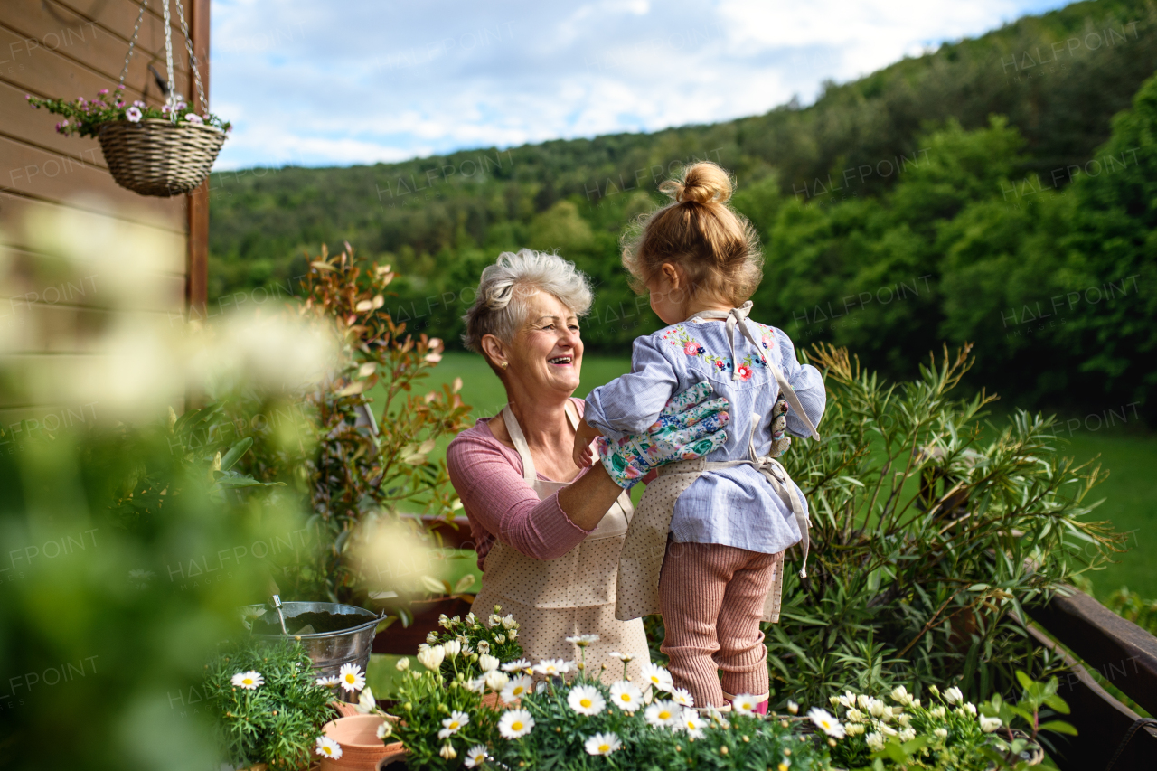 Happy senior grandmother with small granddaughter gardening on balcony in summer.