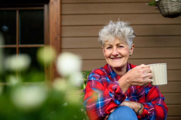 Portrait of senior woman with coffee sitting on terrace in summer, resting.