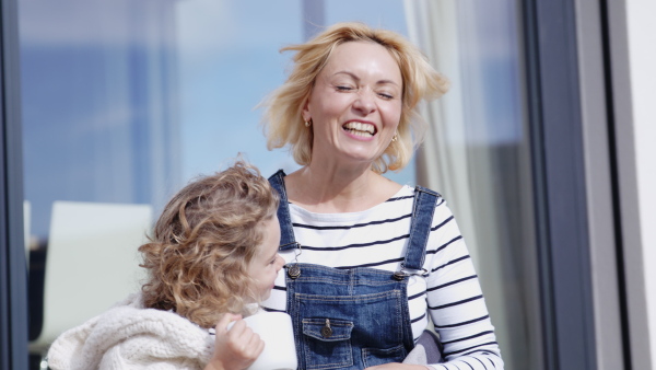 A cute small girl with mother sitting by window on patio outdoors, talking.