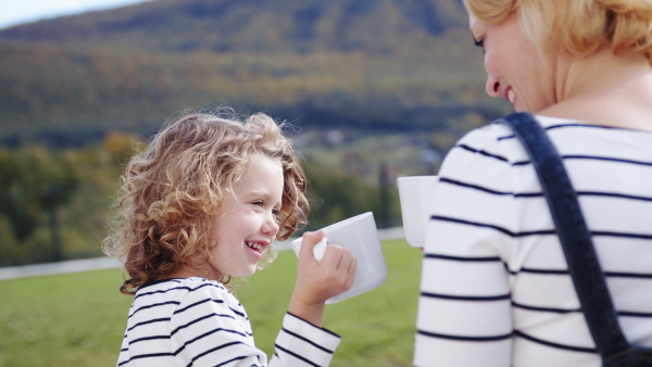 A cute small girl with mother outdoors, clinking cups and talking.