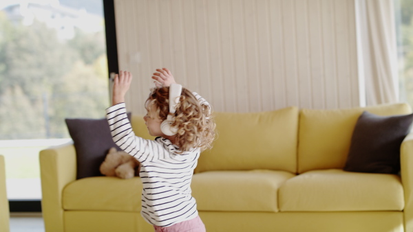 A cheerful cute small girl with headphones indoors at home, spinning.