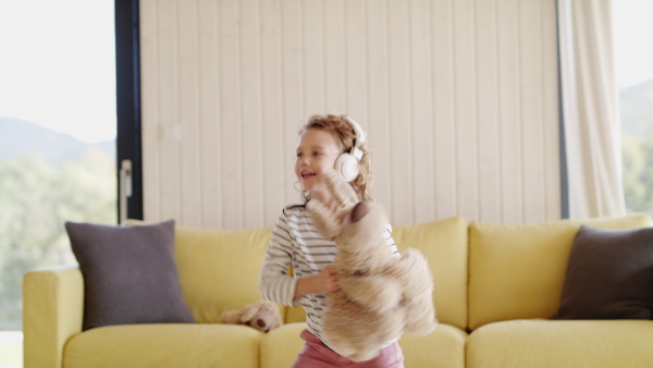 A cheerful cute small girl with headphones indoors at home, jumping.