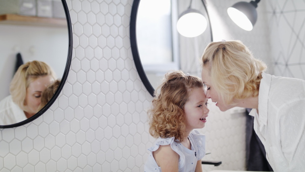 A cute small girl with unrecognizable mother in bathroom indoors at home, talking.