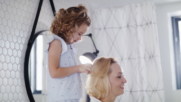 A cute small girl with mother in bathroom indoors at home, braiding hair.