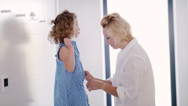 A cute small girl with mother indoors at home, getting dressed and talking.