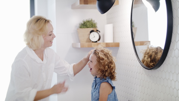 A cute small girl with mother in bathroom indoors at home, talking.