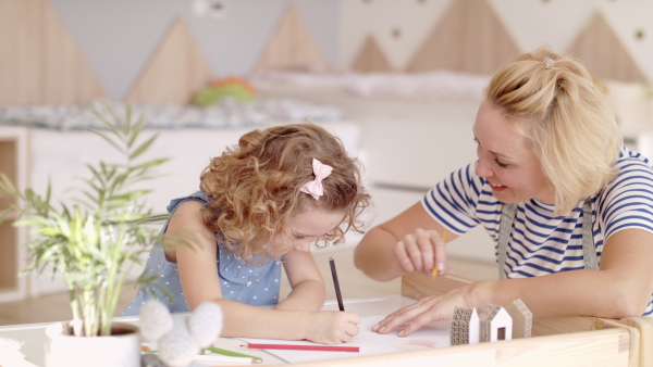 A cute small girl with mother in bedroom indoors at home, drawing pictures.