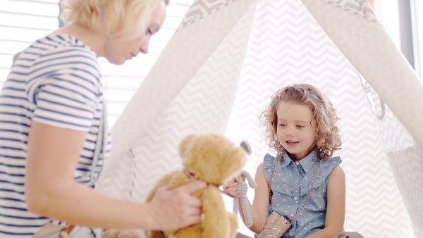 A front view of cute small girl with mother indoors at home, playing.