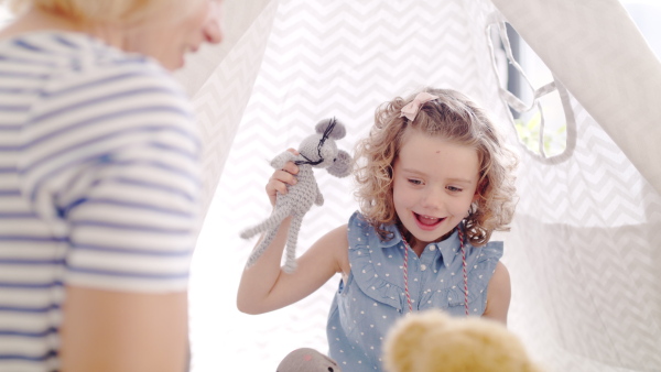 A front view of cute small girl with mother indoors at home, playing.