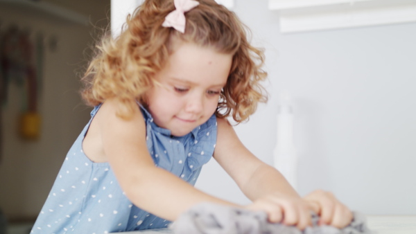 A cute small girl helping with housework indoors at home, cleaning table.