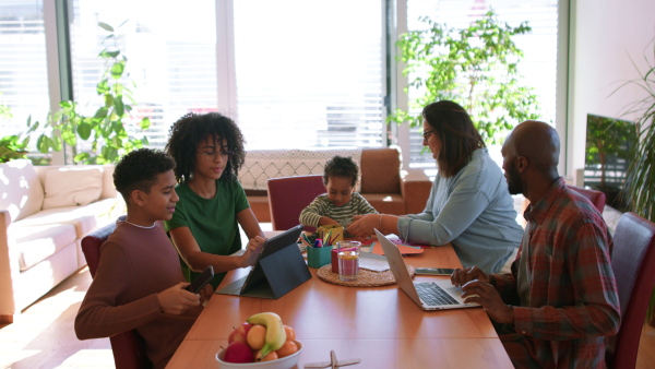 A multiracial family with three children sitting with laptops at table learning and working, homeoffice and homeschool concept.