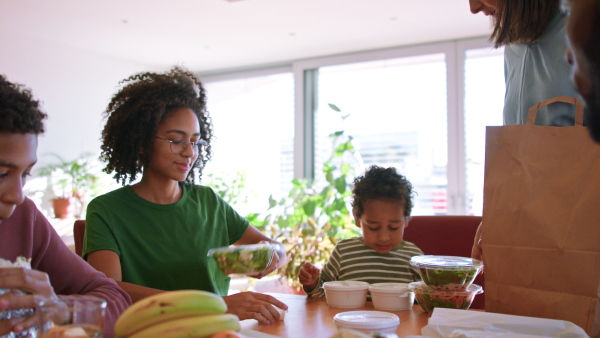 A multiracial family sitting at table and having take away food with children at home.