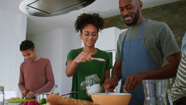 A happy father with his teenage children cooking together in kitchen at home.