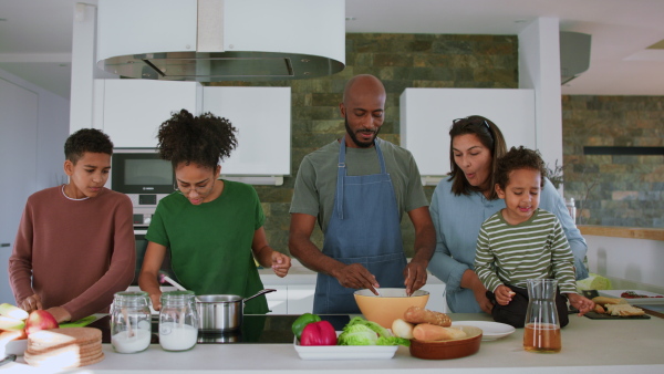 A happy multiracial family with three children cooking together at home.