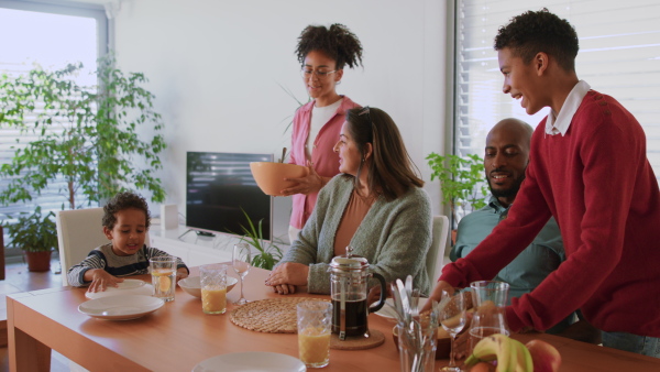 A happy multiracial family sitting at dining table and having lunch at home.