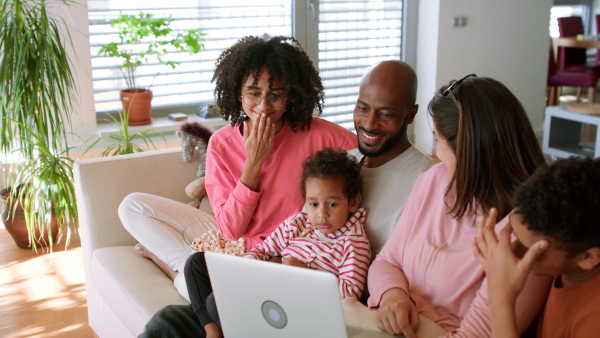 A happy multiracial family sitting on sofa and using laptop at home.