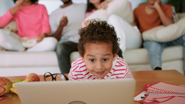 A little multiracial boy using laptop at home with his family at background.