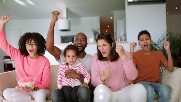 A happy multiracial family with three children sitting on sofa at home and having fun.