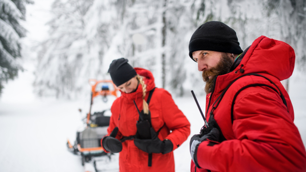 Paramedics from mountain rescue service provide operation outdoors in winter in forest, walking.