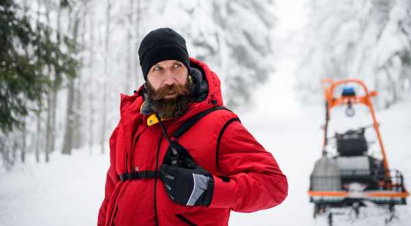 Paramedic man from mountain rescue service with walkie talkie outdoors in a winter in forest.