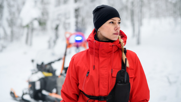 Portrait of woman paramedic from mountain rescue service outdoors in winter in forest.